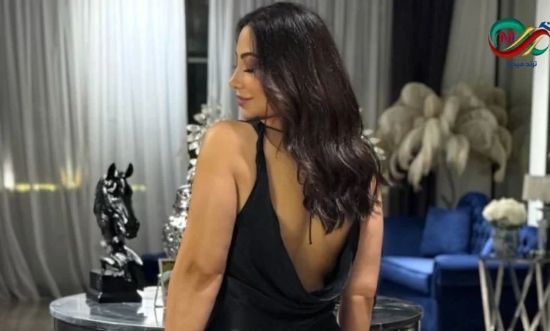 صورة للفنانة بوسي ترتدي فستان أسود طويل مكشوف الظهر مع شعر منسدل على الكتفين خلال جلسة تصوير احترافية.