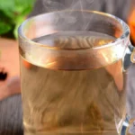 كوب من مشروب عشبي صحي بجانب أعشاب طبيعية تخفض السكر التراكمي مثل القرفة والحلبة.