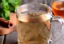 كوب من مشروب عشبي صحي بجانب أعشاب طبيعية تخفض السكر التراكمي مثل القرفة والحلبة.