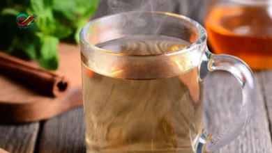 كوب من مشروب عشبي صحي بجانب أعشاب طبيعية تخفض السكر التراكمي مثل القرفة والحلبة.